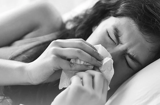 Someone awake in bed, congested and reaching for a tissue